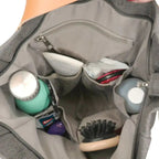 Sac à main gris ouvert avec compartiments organisés, contenant une brosse, des bouteilles, des lunettes et des produits de beauté. Accessoire mode pratique.