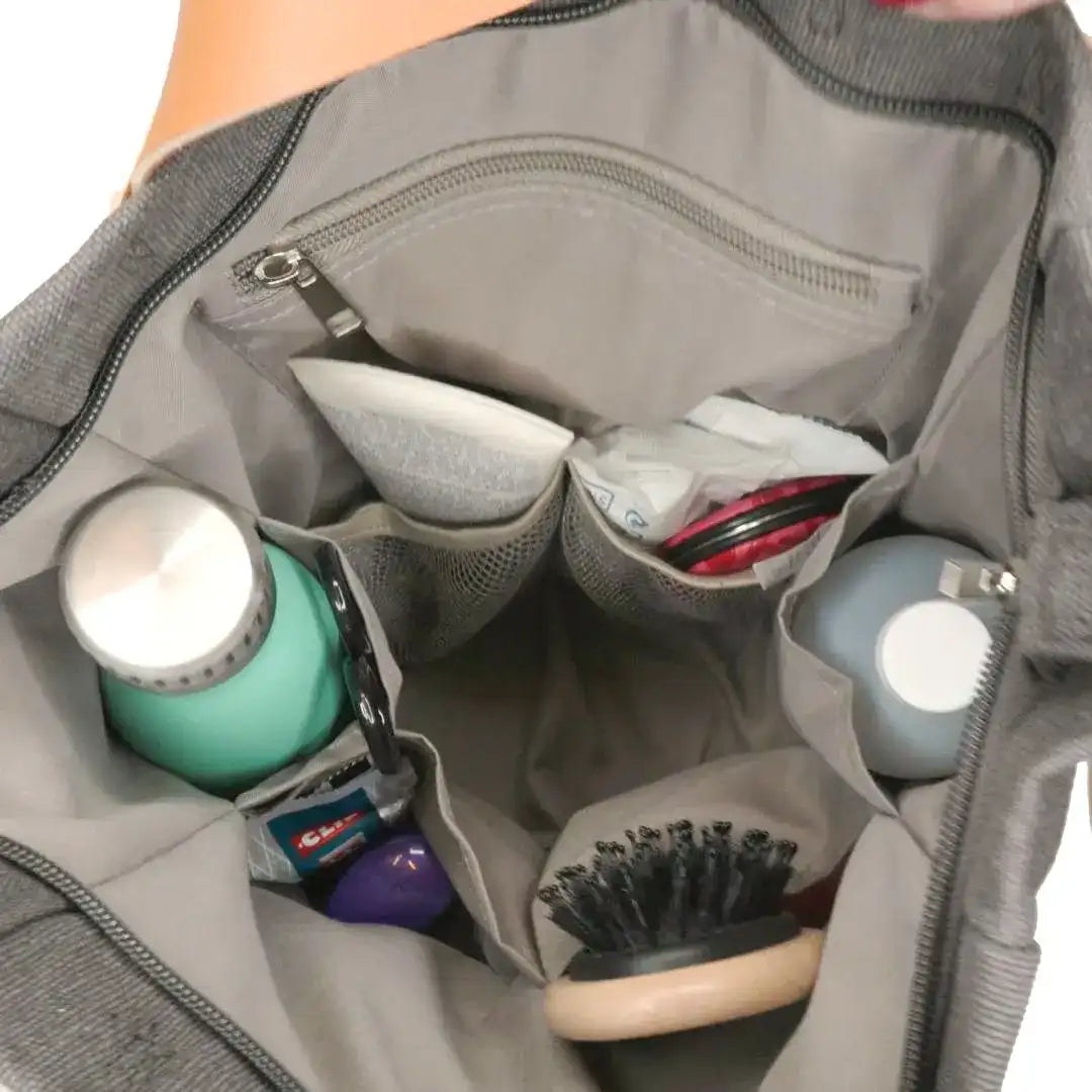 Sac à main gris ouvert avec compartiments organisés, contenant une brosse, des bouteilles, des lunettes et des produits de beauté. Accessoire mode pratique.