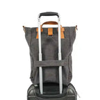 Sac à dos en toile grise fixé sur une valise à roulettes noire, idéal pour le voyage. Design pratique avec poignées en cuir marron.