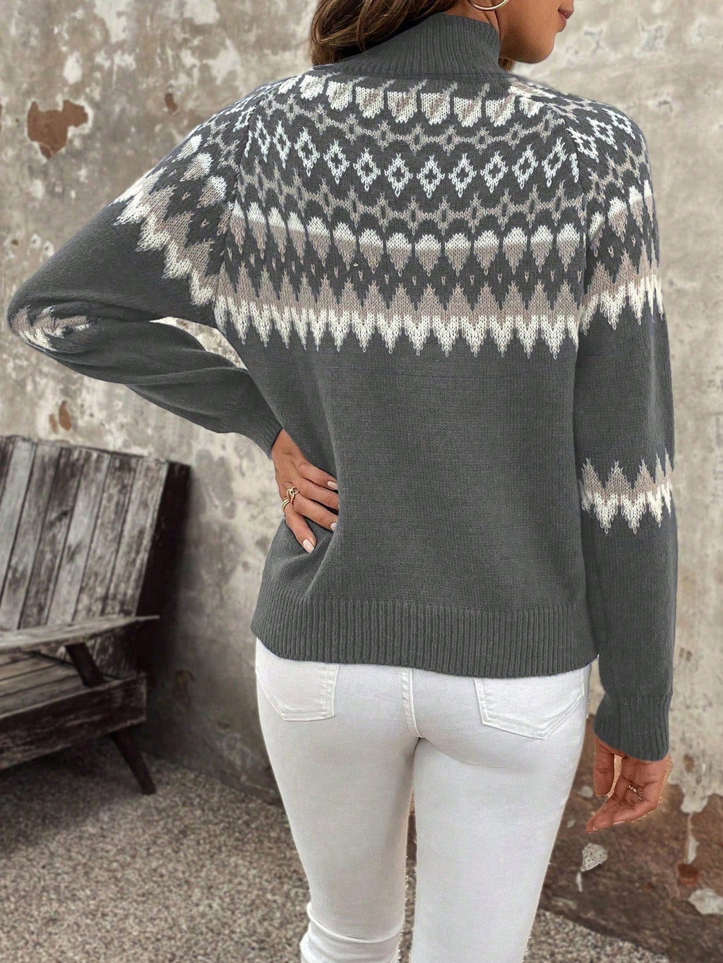 Femme portant un pull gris à motifs nordiques, manches longues, col montant, avec un jean blanc. Style hivernal, mode féminine élégante.