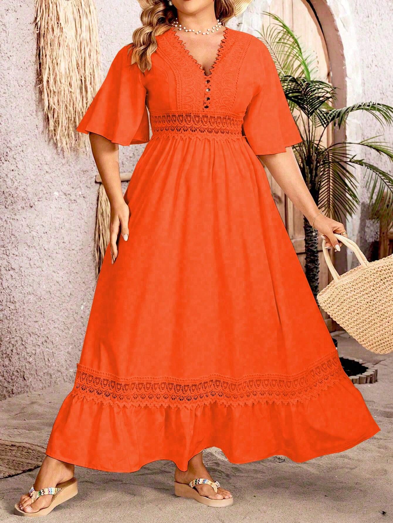 Robe longue orange à manches courtes avec dentelle, portée par une femme tenant un sac en paille, devant un mur texturé et des plantes tropicales.