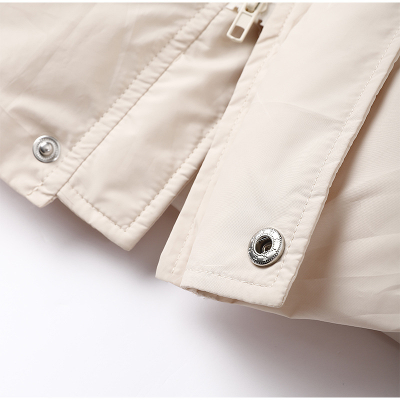 Veste beige en tissu imperméable avec boutons-pression métalliques et fermeture éclair, mode automne-hiver, vêtement extérieur élégant et pratique.
