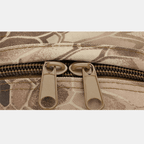 Gros plan sur une fermeture éclair double en métal sur un sac à dos camouflage beige et marron, motif militaire. Accessoire robuste et pratique.