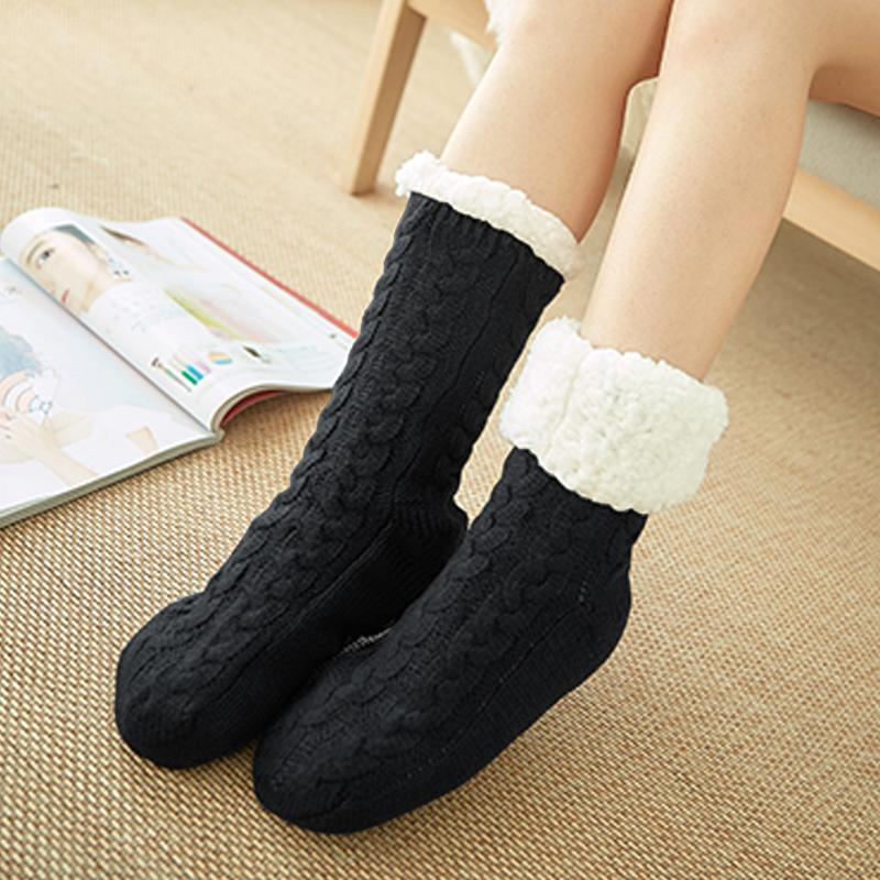 Chaussettes en laine noires avec revers en fourrure blanche, portées sur un tapis beige, à côté d'un magazine ouvert. Confort et chaleur pour l'hiver.