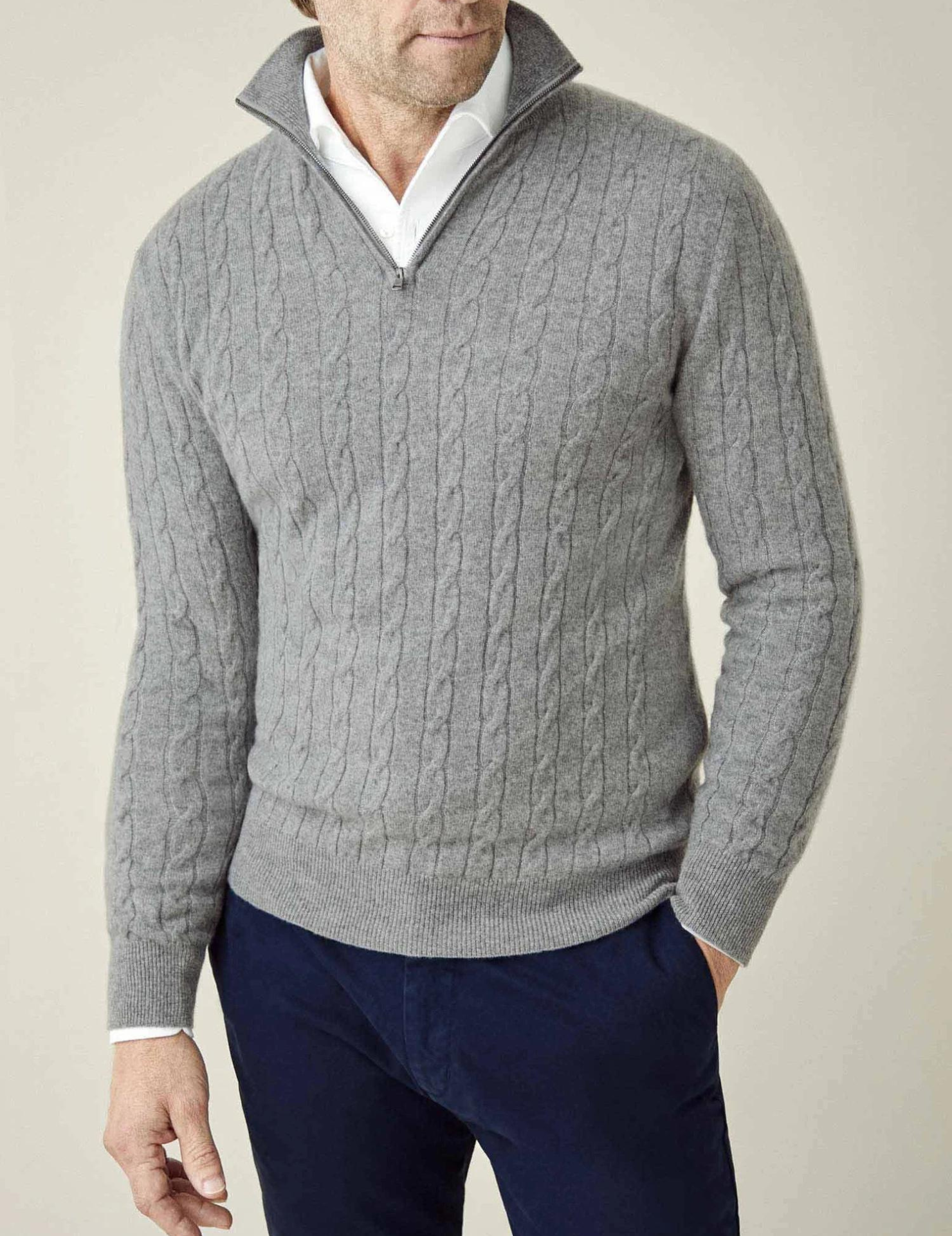 Homme portant un pull gris à col zippé en maille torsadée, chemise blanche en dessous, pantalon bleu marine. Mode masculine élégante et décontractée.