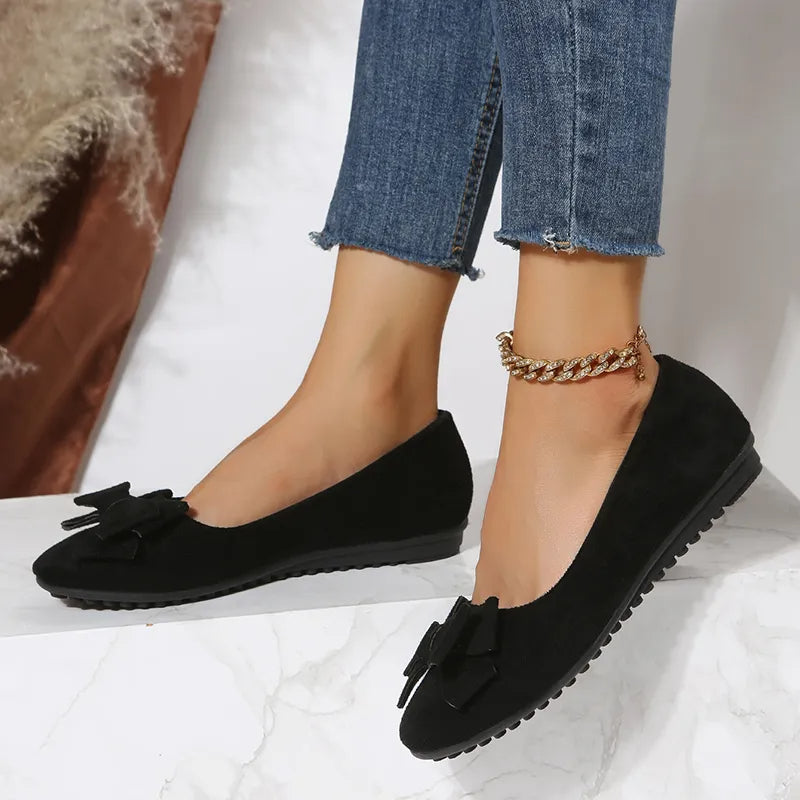 Ballerines noires élégantes avec nœud, portées avec un jean bleu. Chaussures plates tendance pour femme, idéales pour un look chic et décontracté.