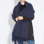 Femme portant une écharpe en laine bleue, ample et à franges, sur un manteau noir. Accessoire d'hiver élégant et chaud. Mode féminine tendance.