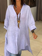 Femme portant une tunique en lin bleu clair, manches longues, avec collier pendentif doré, sur un fond intérieur moderne. Mode décontractée élégante.