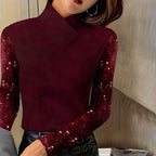 Femme portant un pull bordeaux à manches longues pailletées, posant dans un intérieur moderne. Mode élégante, tendance automne-hiver.