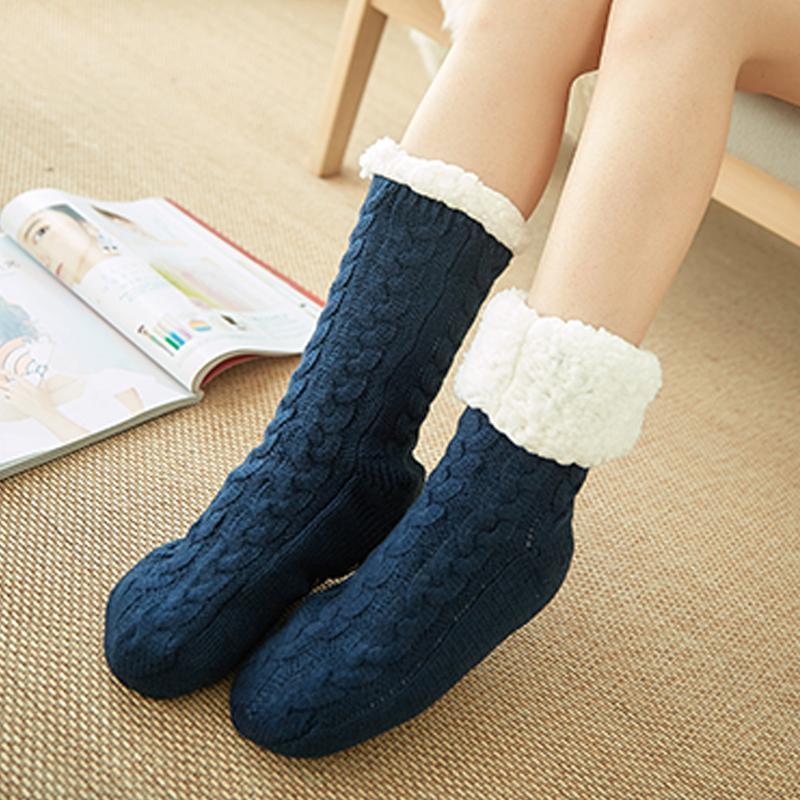 Chaussettes en laine bleue avec revers en fourrure blanche, portées par une personne assise sur un tapis beige, magazine ouvert à côté.