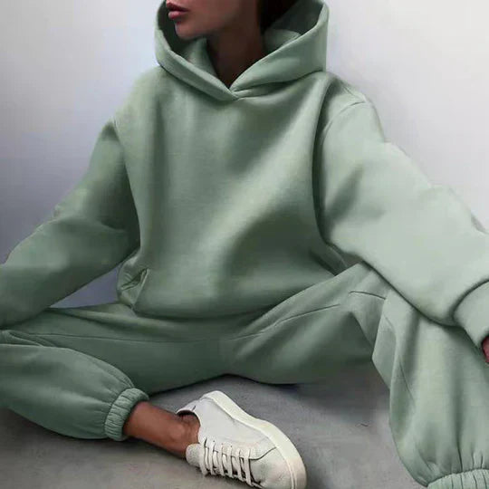 Personne portant un survêtement vert menthe avec capuche, assise, baskets blanches. Mode décontractée, tendance streetwear, confort moderne.