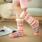 Chaussettes roses en laine avec motifs nordiques, portées par une personne assise sur un canapé, magazine ouvert au sol. Confort et style hivernal.