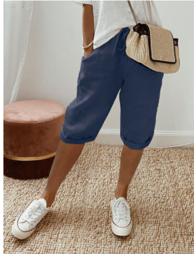 Femme portant un short bleu, t-shirt blanc, baskets blanches et sac en osier. Mode décontractée, tendance estivale, style confortable.