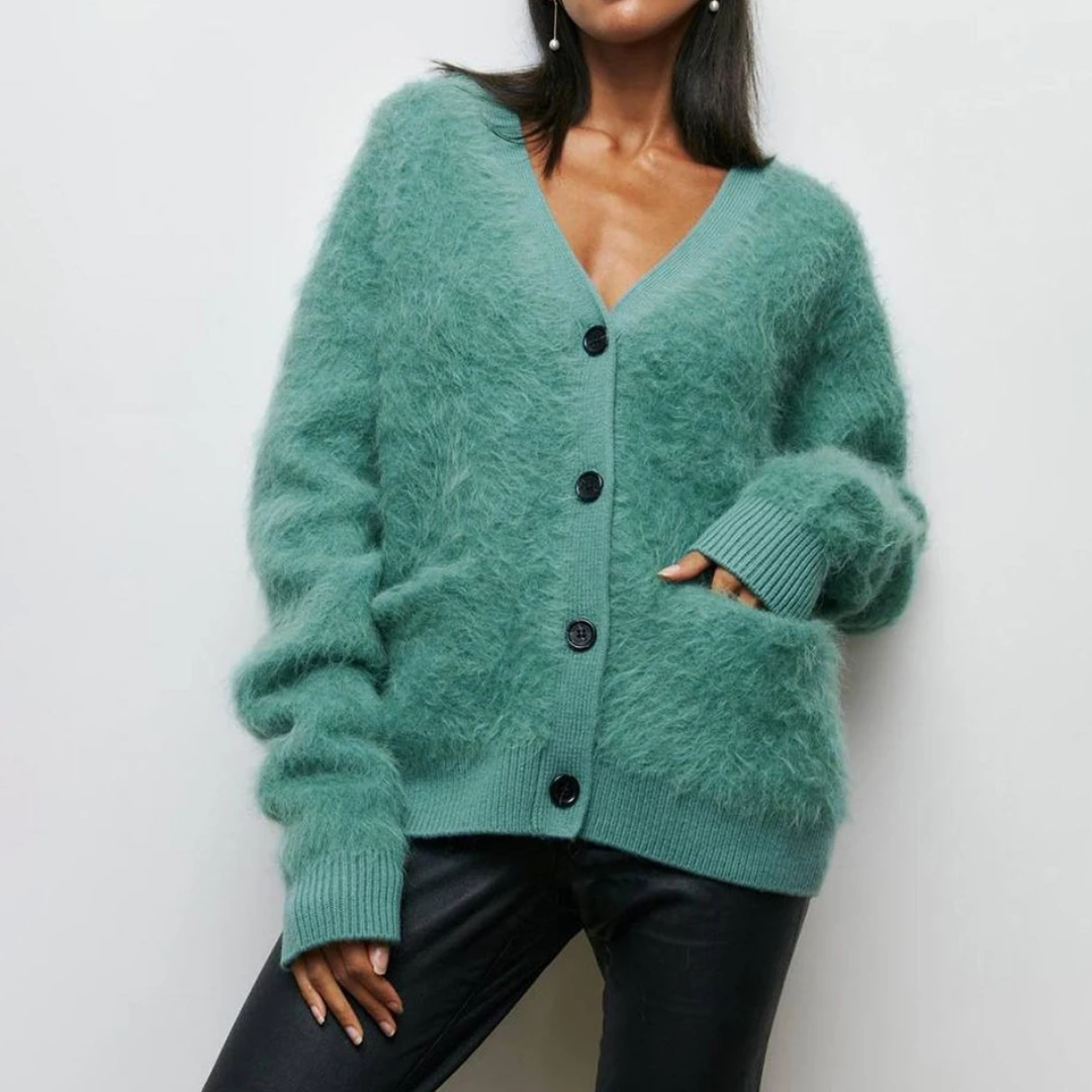Femme portant un cardigan vert en mohair avec boutons noirs, manches longues, col en V, associé à un pantalon noir. Mode automne-hiver élégante.