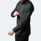 Homme portant une chemise noire ajustée, manches longues, sur fond blanc. Mode masculine élégante, tenue formelle, style moderne.
