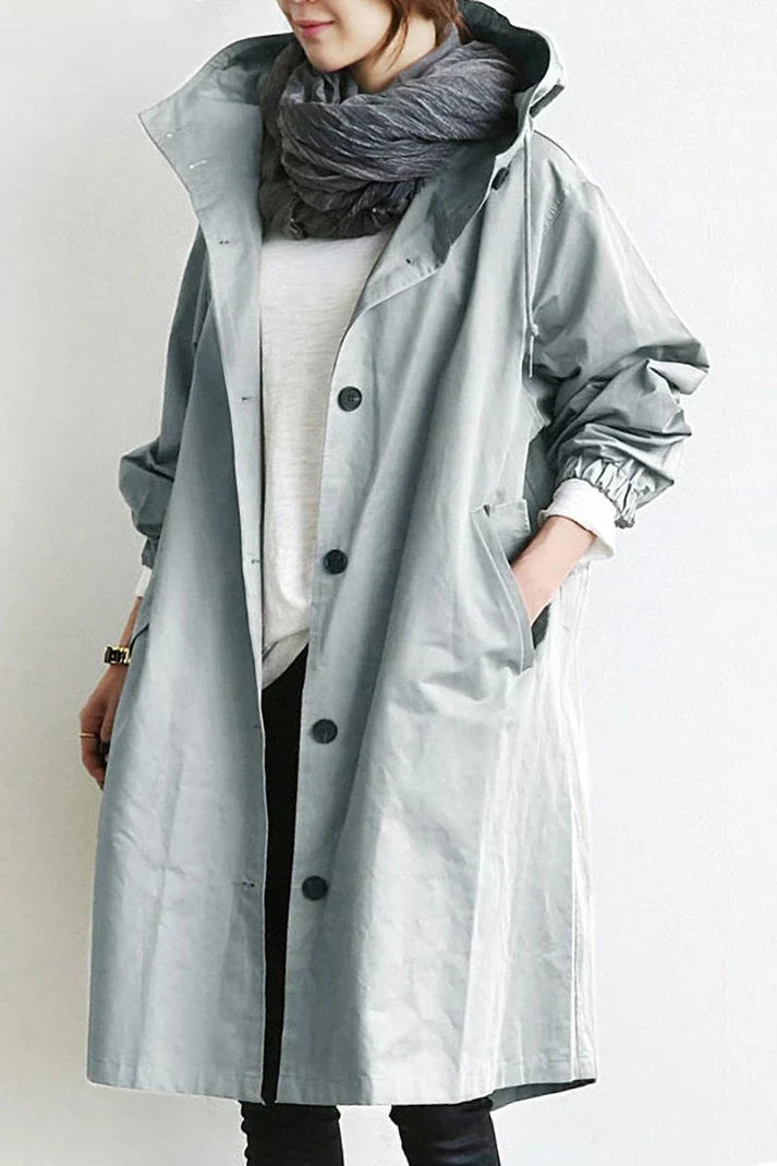 Femme portant un imperméable gris clair avec écharpe grise, chemise blanche et pantalon noir. Mode automne, style décontracté, tendance vestimentaire.