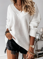 Femme portant un pull blanc en maille avec un col en V, associée à un short noir à franges. Accessoires dorés et montre élégante.