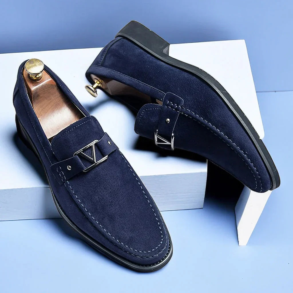 Chaussures mocassins en daim bleu marine pour homme avec boucle métallique, posées sur fond bleu et blanc. Élégance, mode masculine, chaussures de luxe.