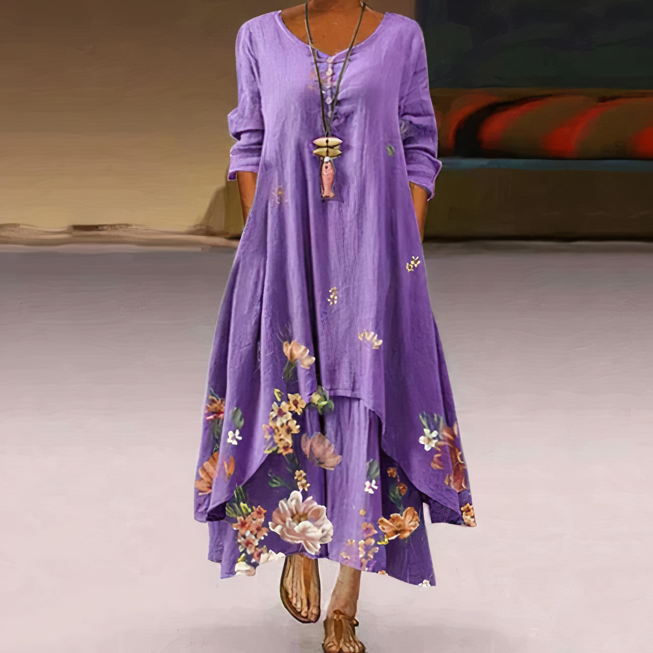 Robe longue violette à manches longues avec motifs floraux, col rond, portée par une femme. Style bohème chic, idéal pour l'été.
