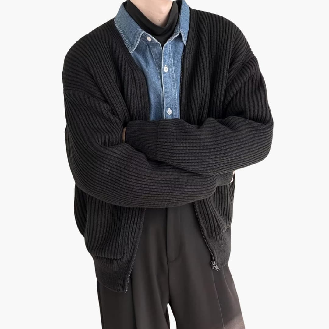 Personne portant un cardigan noir en maille sur une chemise en jean, bras croisés. Mode automne-hiver, style décontracté et élégant.