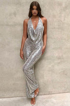 Femme portant une combinaison argentée à paillettes, posant contre un mur beige. Mode élégante, tenue de soirée glamour, style chic et tendance.