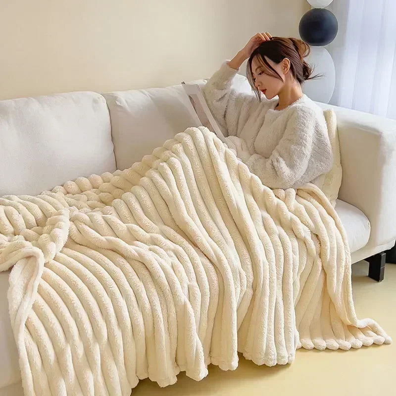 Femme lisant sur un canapé, enveloppée dans une couverture en fausse fourrure beige. Ambiance cosy, détente à la maison, confort hivernal.