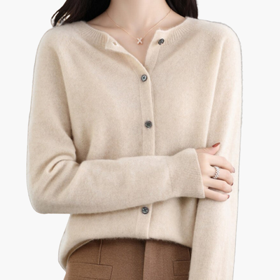 Femme portant un cardigan beige en cachemire avec boutons, collier délicat et pantalon marron. Mode élégante, tenue automne-hiver, style chic.