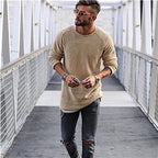 Jeune homme à la mode portant un pull beige et un jean déchiré, marchant sur un pont moderne. Style urbain, lunettes de soleil, look décontracté.