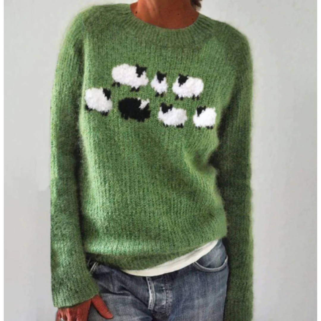 Pull vert en laine avec motif moutons noirs et blancs, manches longues, porté par une personne en jean. Mode automne-hiver, style décontracté.