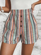Short en lin rayé multicolore avec boutons, femme posant sur fond de mur blanc. Mode estivale, style décontracté, tendance 2023.