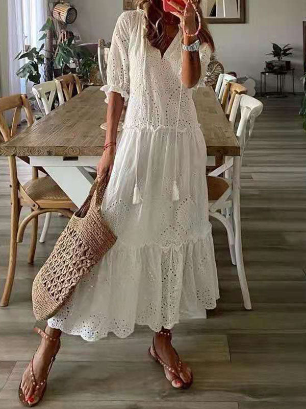 Robe blanche en dentelle bohème portée par une femme avec un sac en osier, debout dans une salle à manger moderne avec table en bois et chaises blanches.