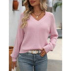 Femme portant un pull rose en maille avec col en V, manches ajourées, et un jean bleu. Style décontracté, mode féminine tendance, look automne.