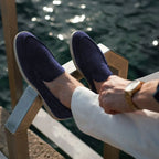 Chaussures mocassins en daim bleu marine portées avec un pantalon blanc, vue au bord de l'eau. Style élégant et décontracté pour homme.