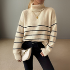 Femme portant un pull à col roulé beige rayé, avec un collier doré et un sac à main blanc. Mode automne, style décontracté chic.