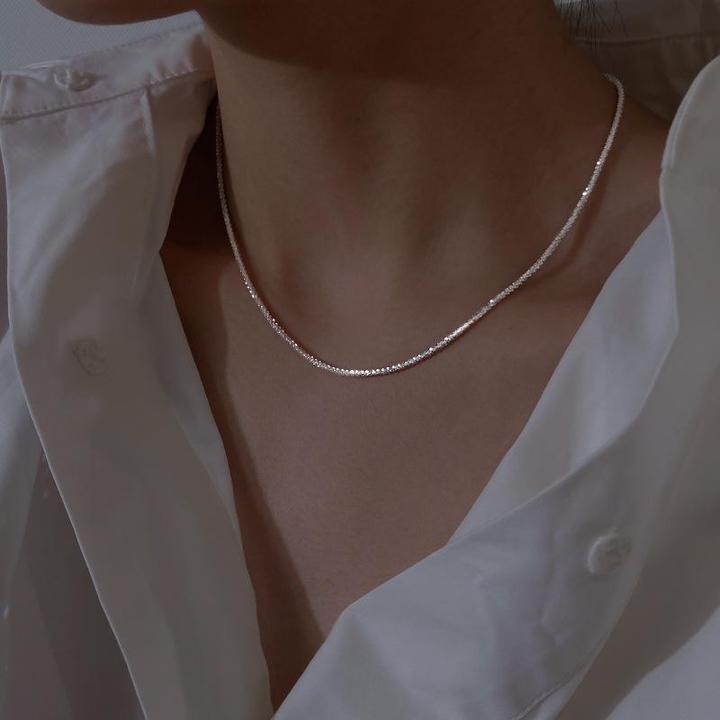 Collier en argent délicat sur un cou, porté avec une chemise blanche élégante. Bijoux minimalistes, mode féminine, accessoire tendance.