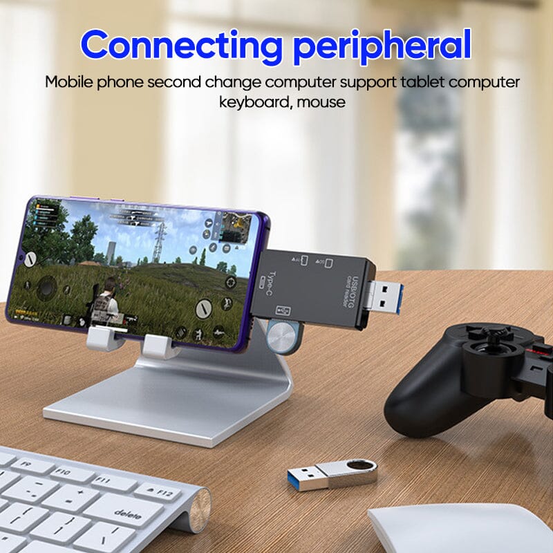 Support de téléphone portable en aluminium avec smartphone affichant un jeu, connecté à un adaptateur USB, clavier et manette sur bureau en bois.
