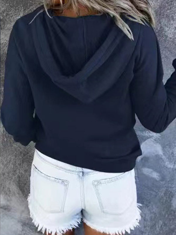Femme en sweat à capuche noir et short en jean blanc, vue de dos. Mode décontractée, tenue estivale, style urbain.