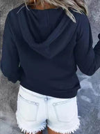 Femme en sweat à capuche noir et short en jean blanc, vue de dos. Mode décontractée, tenue estivale, style urbain.