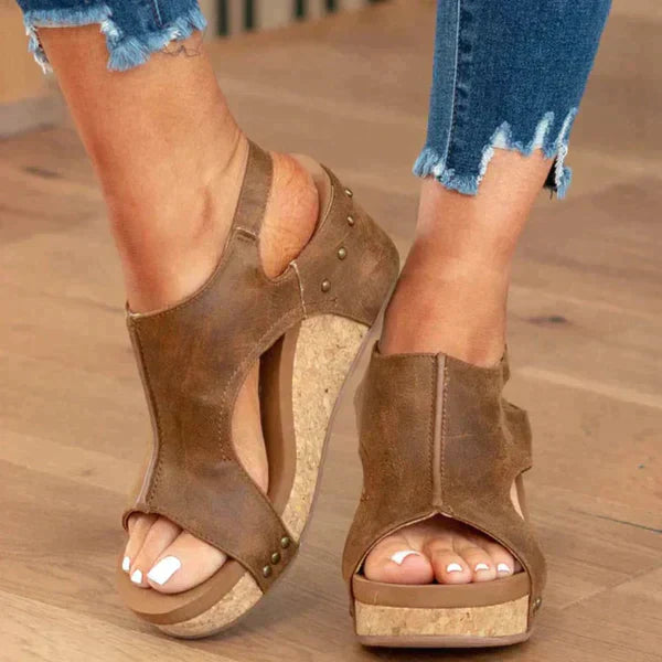 Sandales compensées en cuir marron avec clous, portées avec un jean déchiré. Chaussures d'été tendance pour femmes, confortables et élégantes.