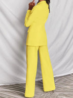 Femme en tailleur pantalon jaune vif, veste ajustée, pantalon large, pose de dos. Mode élégante, tendance, tenue professionnelle féminine.