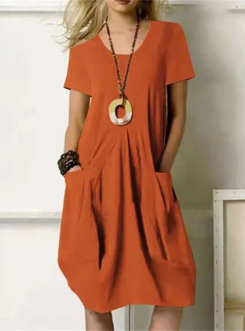 Robe orange ample avec poches, collier pendentif circulaire, femme blonde. Mode décontractée, tendance été, style chic et confortable.