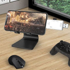 Smartphone sur support avec clé USB connectée, affichant un jeu vidéo de science-fiction; souris et manette de jeu sur bureau en bois.