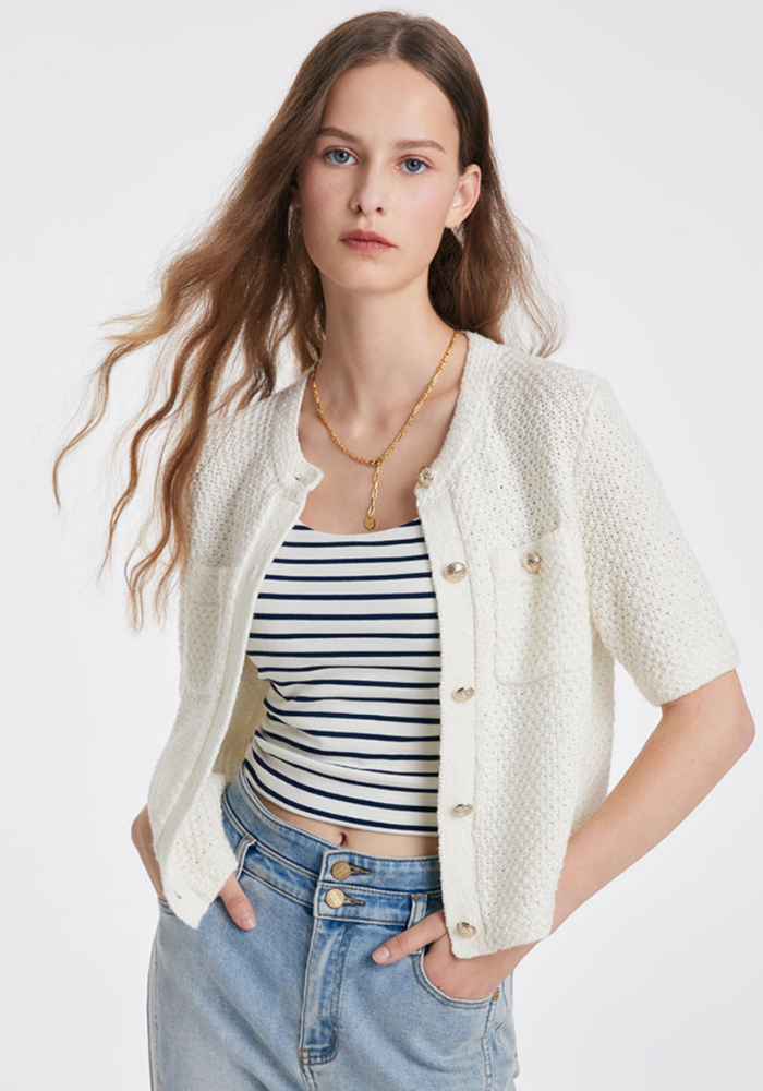 Femme portant un cardigan blanc en tricot avec boutons, t-shirt rayé noir et blanc, et jean bleu clair. Mode féminine élégante et décontractée.