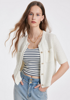 Femme portant un cardigan blanc en tricot avec boutons, t-shirt rayé noir et blanc, et jean bleu clair. Mode féminine élégante et décontractée.