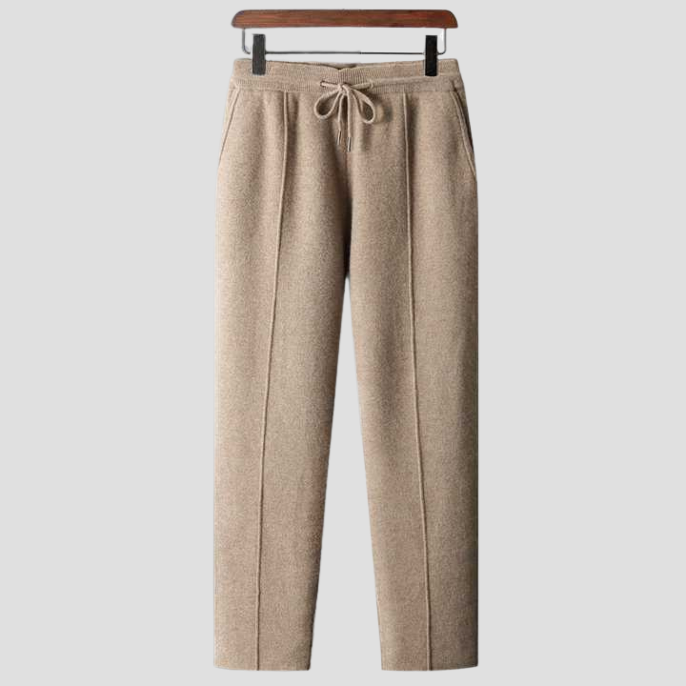 Pantalon en laine beige pour femme, coupe droite, avec cordon de serrage à la taille, suspendu sur un cintre en bois. Mode automne-hiver élégante.
