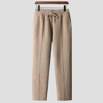 Pantalon en laine beige pour femme, coupe droite, avec cordon de serrage à la taille, suspendu sur un cintre en bois. Mode automne-hiver élégante.