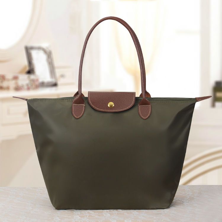 Sac à main en toile vert olive avec poignées en cuir marron, posé sur une table. Accessoire de mode élégant et pratique pour femme.