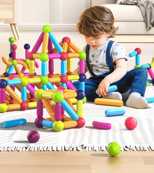 Enfant jouant avec des blocs de construction magnétiques colorés sur un tapis blanc dans un salon lumineux. Jouets éducatifs, développement enfant.