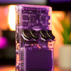 Console de jeu rétro transparente avec boutons noirs, circuits visibles, éclairage d'ambiance violet et orange, plante en arrière-plan.