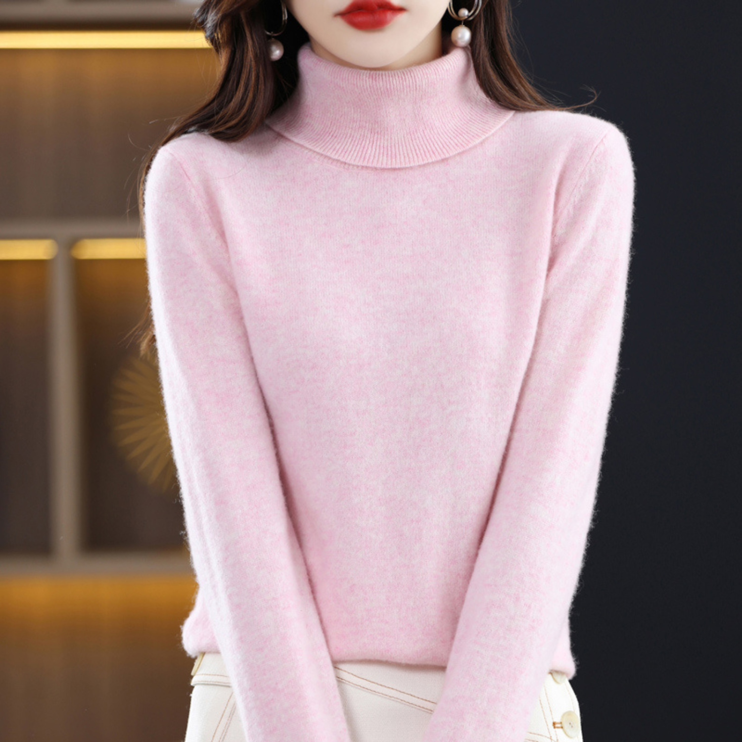 Femme portant un pull rose à col roulé, élégante et moderne, mode automne-hiver, style décontracté chic, fond intérieur flou.